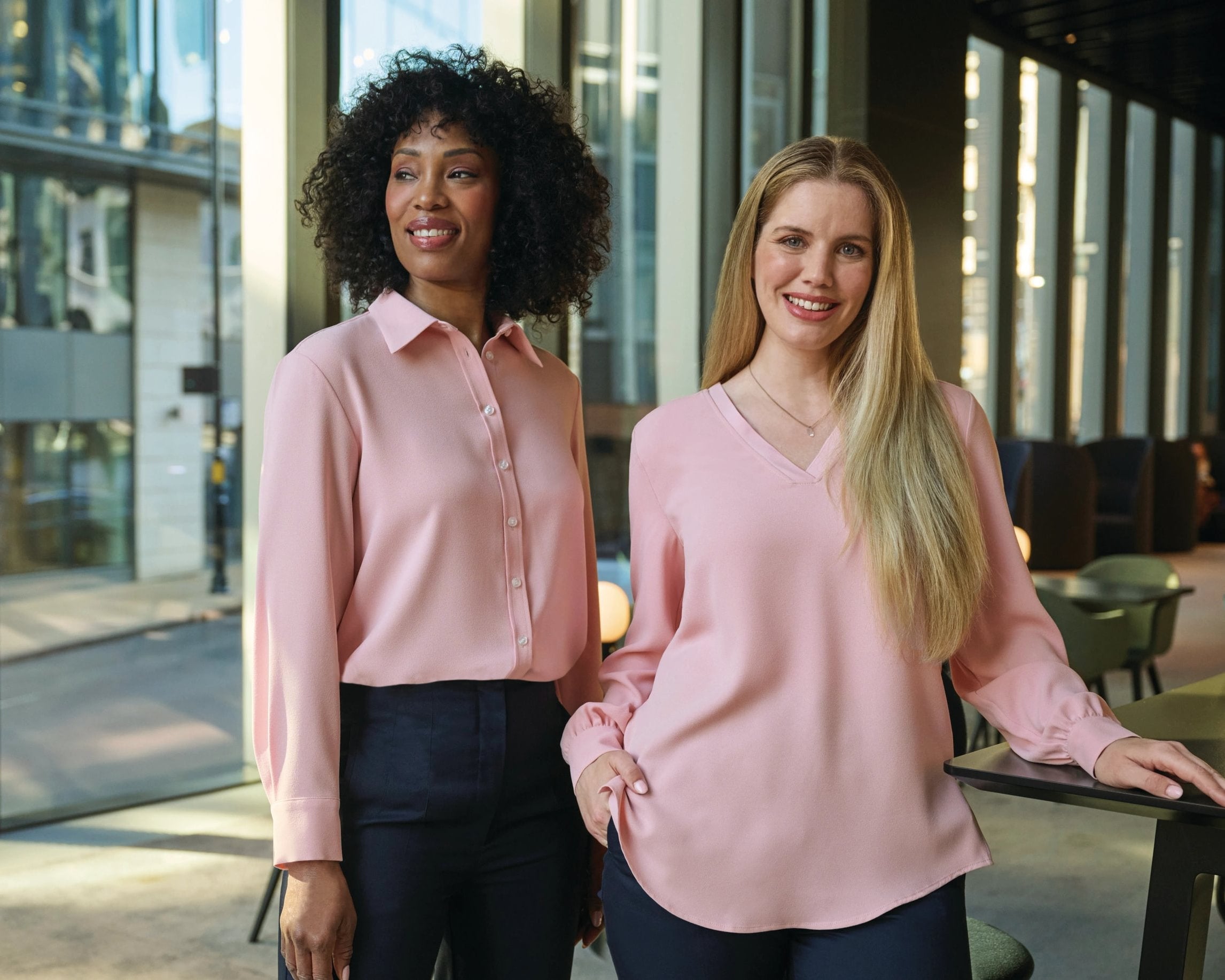 Two women wearing Pink Brook Taverner Womens Workwear Blouses. They are stood in Manchester in a hotel bar area