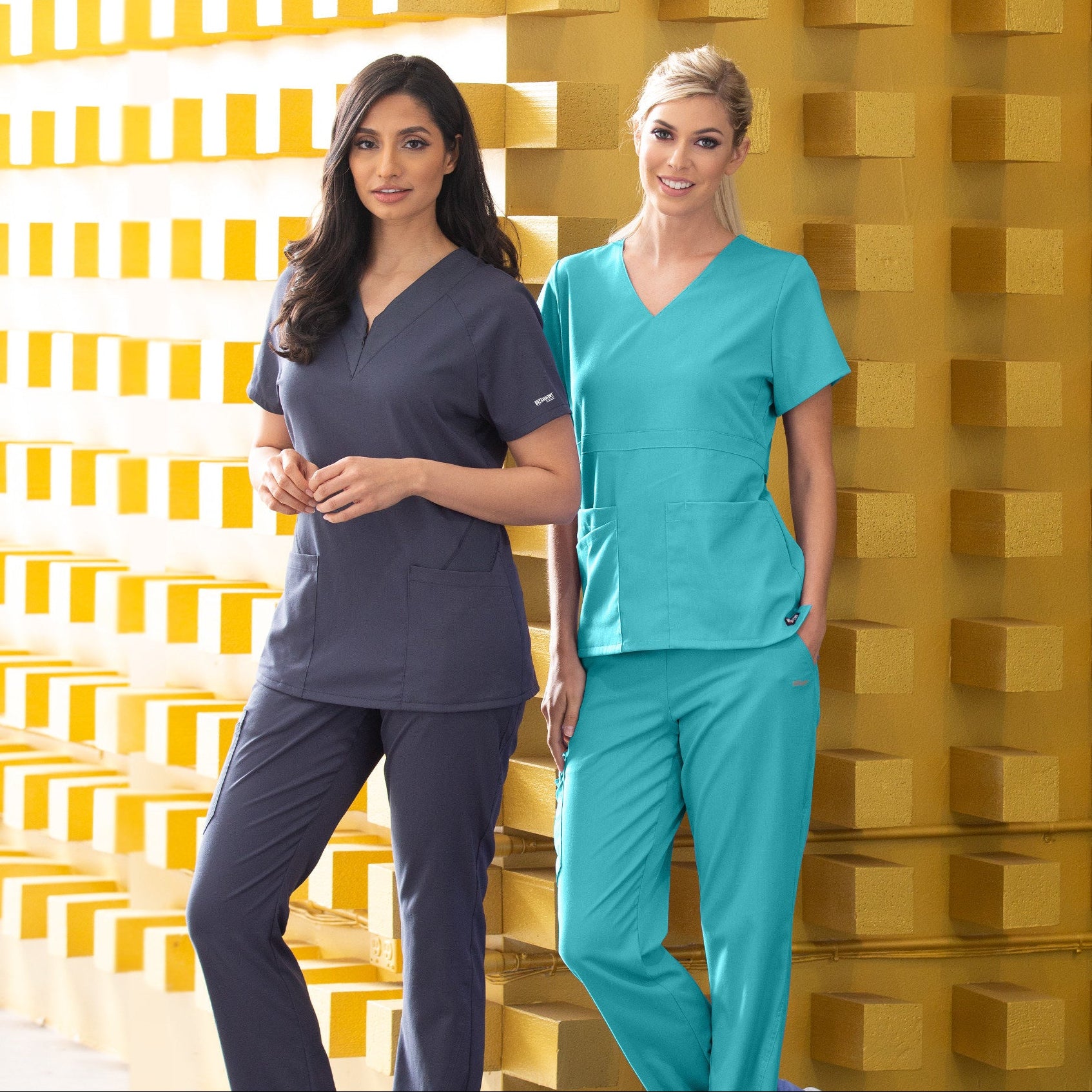 Two individuals wearing medical scrubs against a yellow geometric patterned wall.