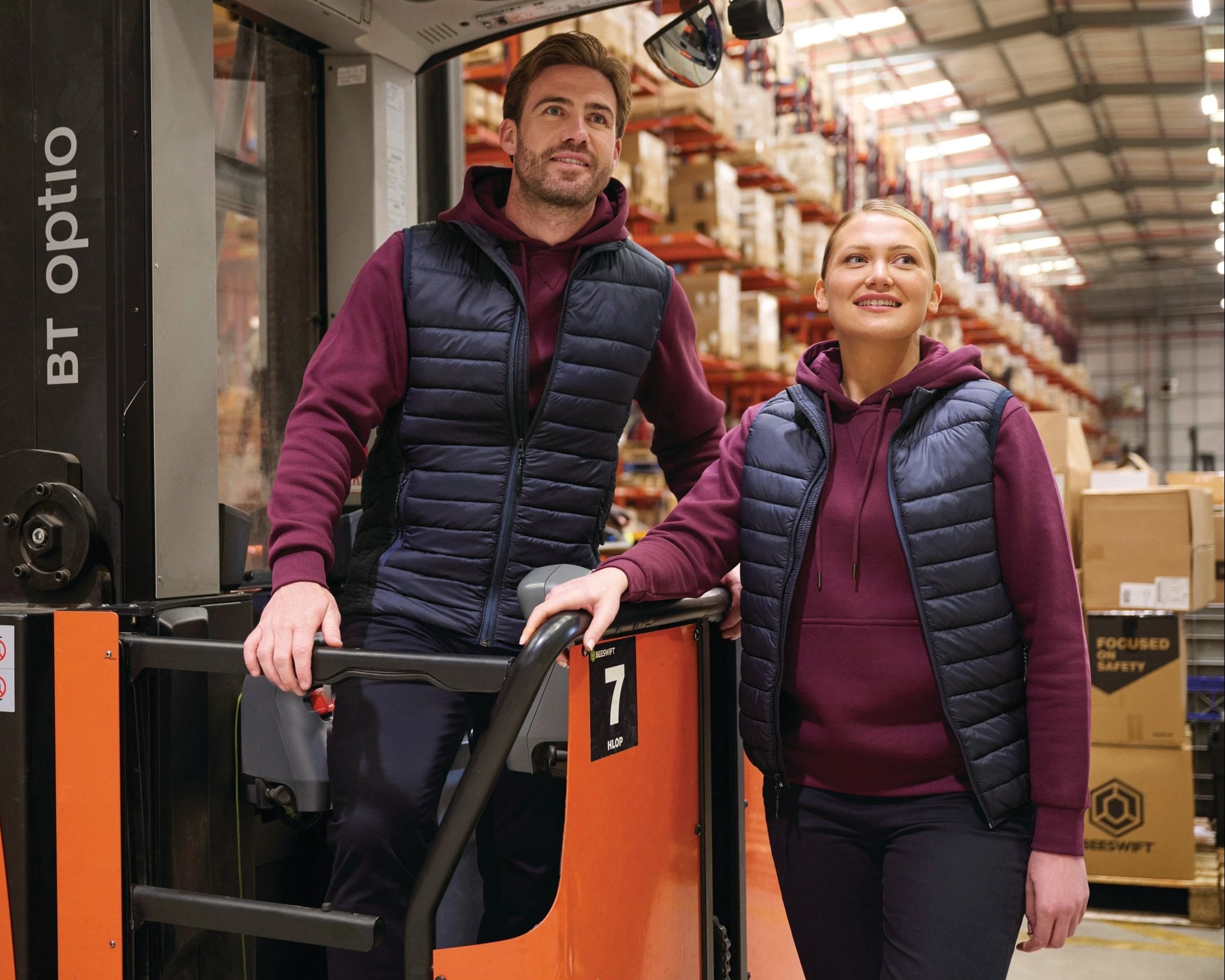 Two people standing next to a forklift in a warehouse.